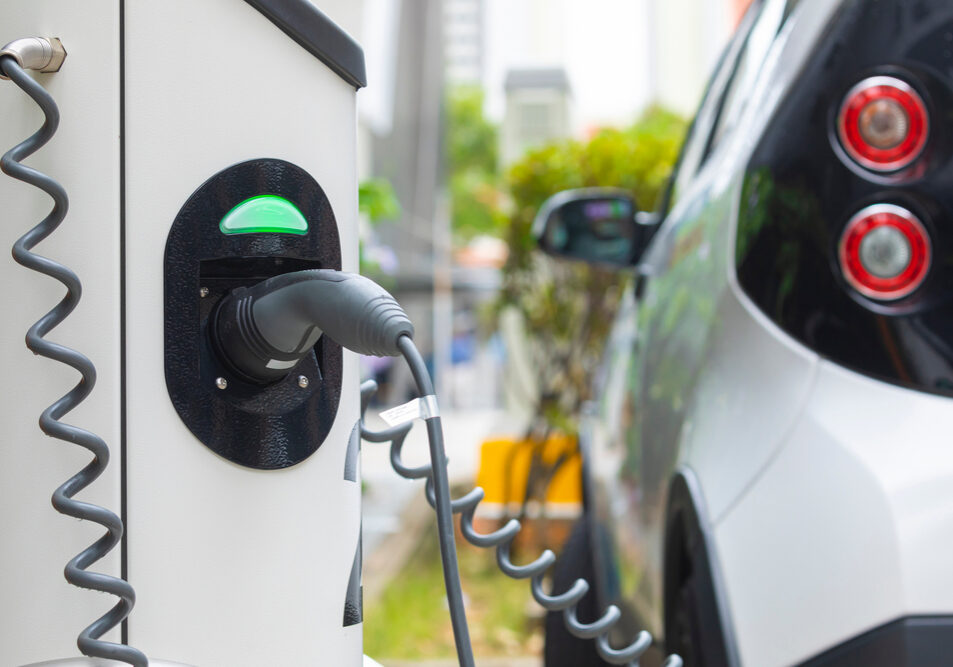 A modern residential garage featuring a home electric vehicle charging station plugged into a clean electric car, displaying a green readiness indicator light.